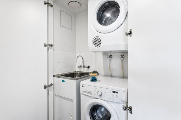 A compact laundry area with a washing machine, a sink, and a dryer. - Lux Waterfront - Prime Location Pool Gym Sauna (Cairns)