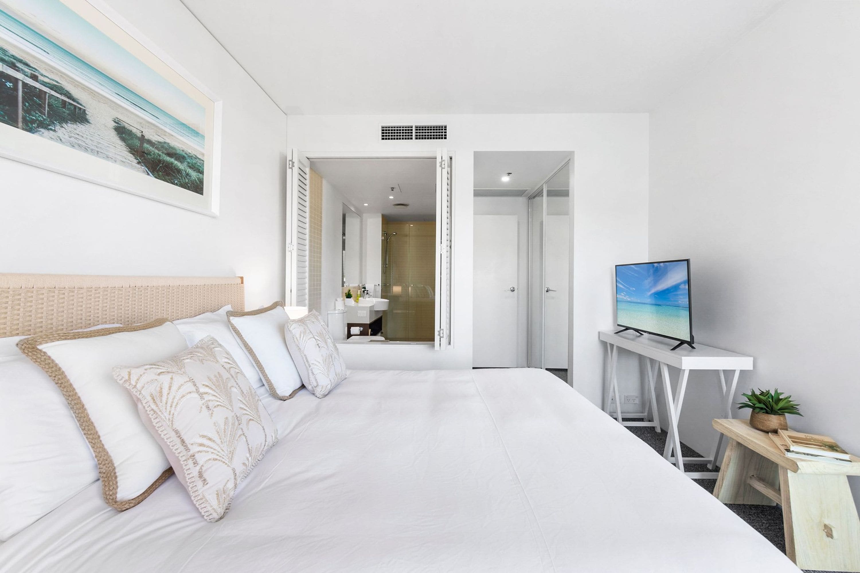 Habitación de hotel con una cama grande, un televisor, un escritorio pequeño y un baño visible a través de una puerta abierta.
