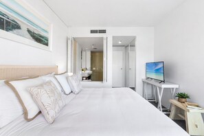 Une chambre d’hôtel avec un grand lit, une télévision, un petit bureau et une salle de bain visible à travers une porte ouverte.