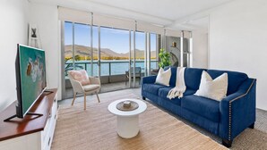 A modern living room with a blue sofa, a white coffee table, and a painting on the wall. - Lux Waterfront - Prime Location Pool Gym Sauna (Cairns)