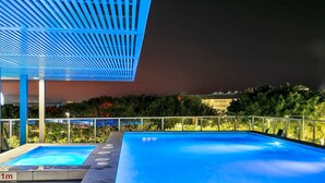 Una piscina sul tetto illuminata di blu, circondata da vegetazione e una ringhiera in vetro.