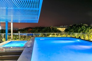 A rooftop pool with a blue-lit canopy, surrounded by greenery and a glass railing. - Lux Waterfront - Prime Location Pool Gym Sauna (Cairns)