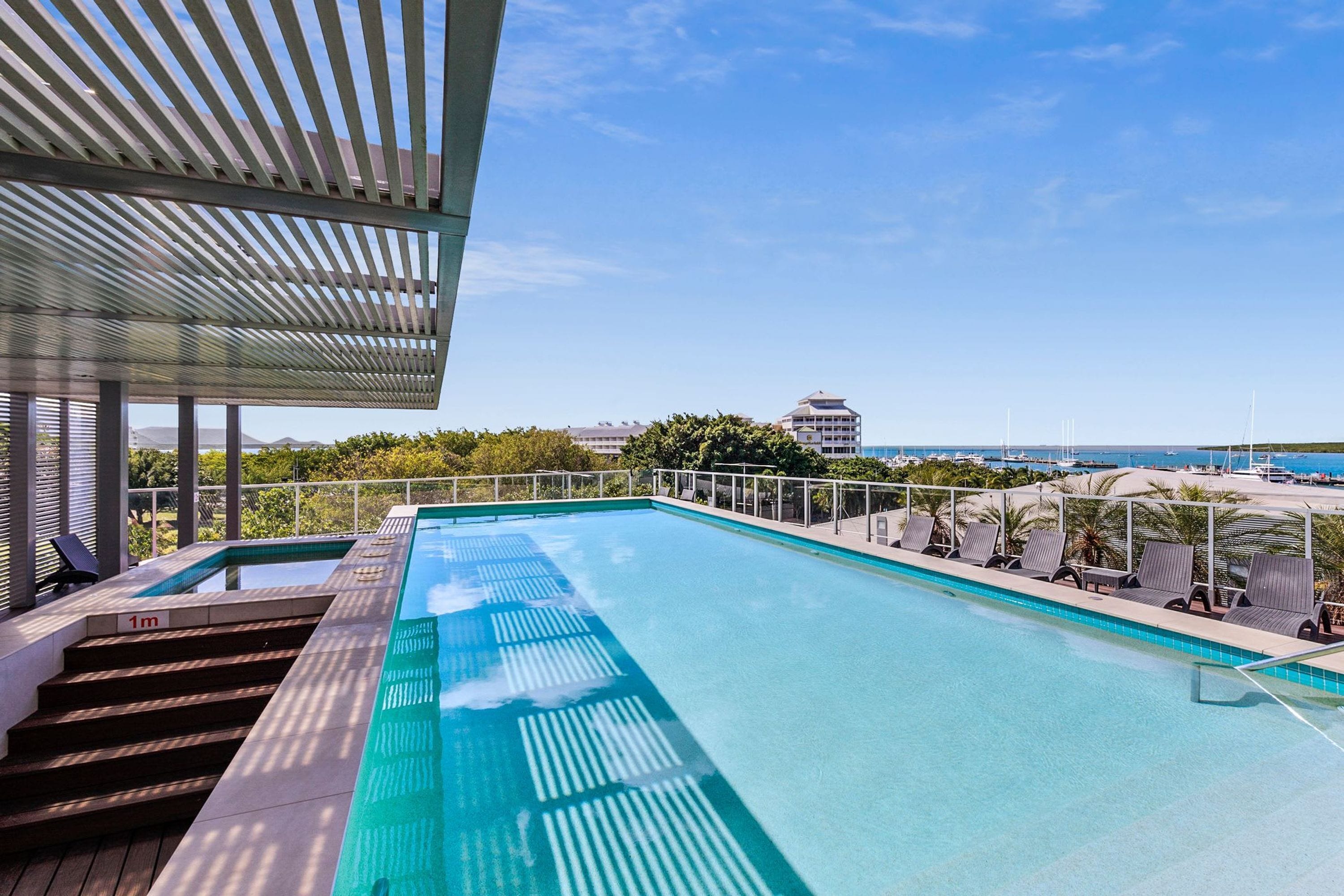 Piscina infinita no terraço com vista clara do oceano e edifícios ao fundo.