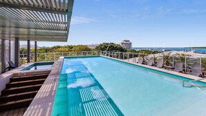A rectangular swimming pool with a clear blue water surface, surrounded by a deck with lounge chairs and a pergola structure.