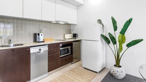 A modern kitchen with white cabinets, a Bosch dishwasher, a microwave, a Samsung refrigerator, and a potted plant. - Lux Waterfront - Prime Location Pool Gym Sauna (Cairns)