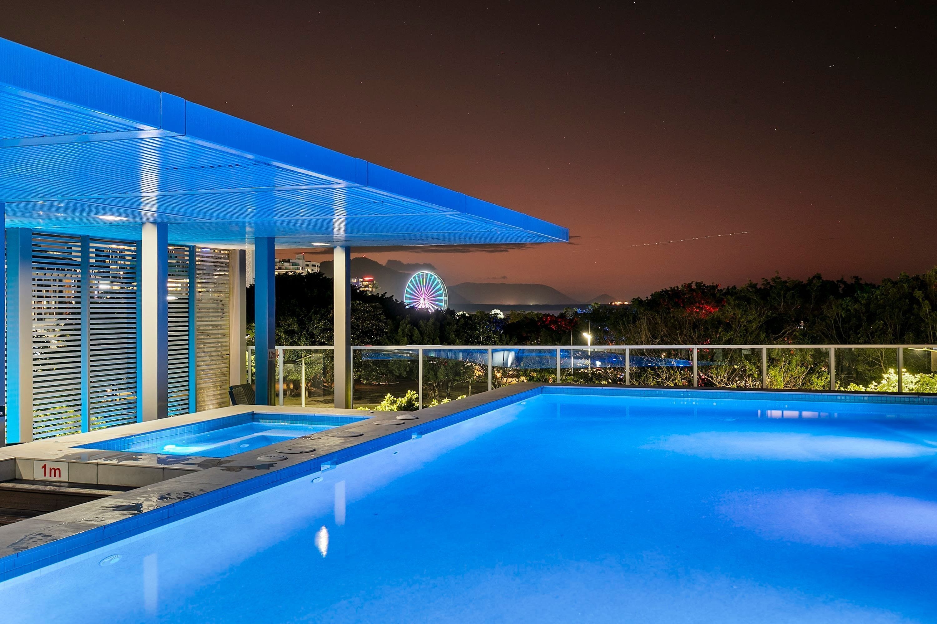Un espace piscine extérieur moderne offrant une vue dégagée sur une grande roue en arrière-plan.