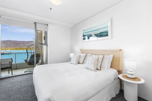 A hotel room with a large bed, a view of the sea, a balcony with a chair, and a framed picture on the wall. - Lux Waterfront - Prime Location Pool Gym Sauna (Cairns)
