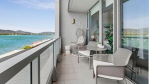A balcony with a view of the sea, two wicker chairs, a small table, and a potted plant.