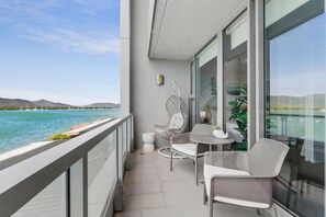 A balcony with a view of the sea, wicker furniture, and a small table with a plant. - Lux Waterfront - Prime Location Pool Gym Sauna (Cairns)