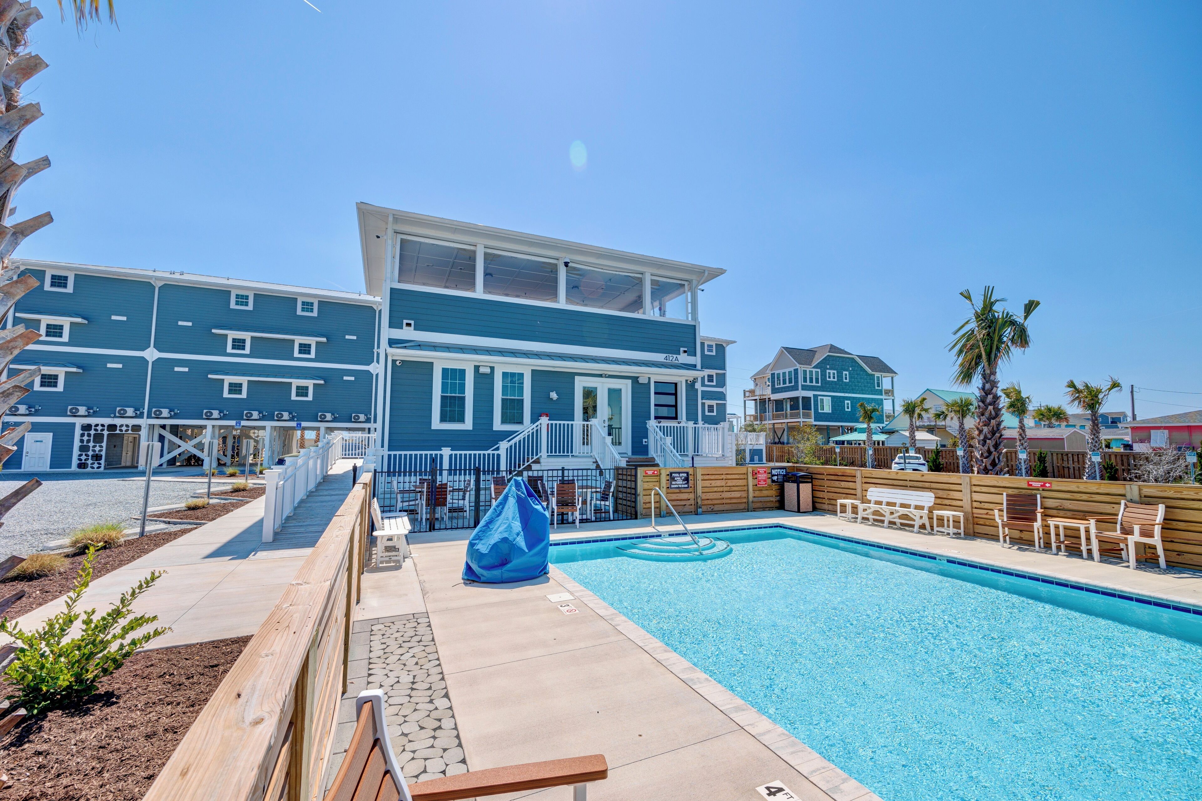 A pool area with a wooden deck, lounge chairs, and a building with multiple windows and balconies.