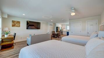 A hotel room with two beds, a desk with a lamp, a chair, a dining table, and a TV on the wall.