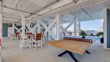 An indoor recreational area with a ping pong table, white chairs, and a view of the outside.