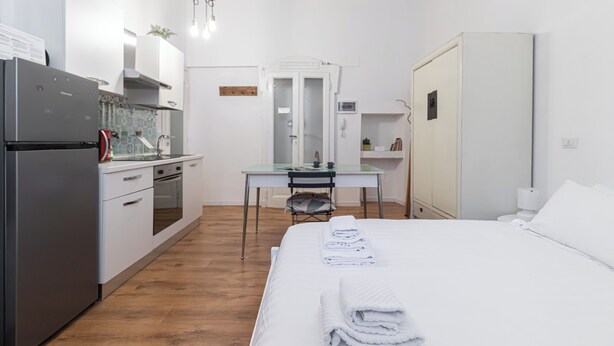 Ett kompakt hotellrum med ett litet pentry, en säng med prydligt hopvikta handdukar, ett skrivbord och en garderob.