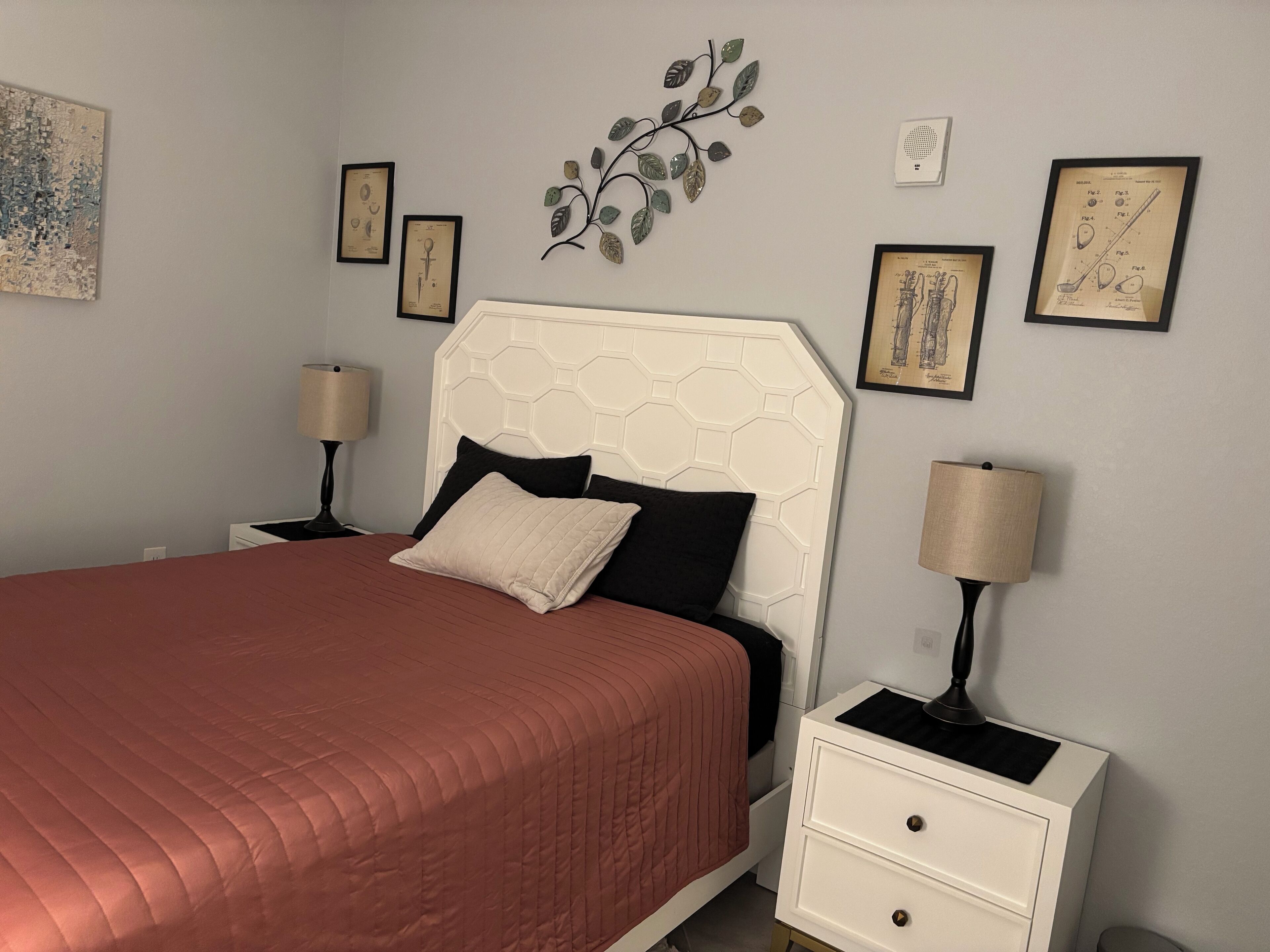 Ein ordentlich eingerichtetes Schlafzimmer mit einem Bett, zwei Nachttischen und einer Wanddekoration in Form eines Blattes.