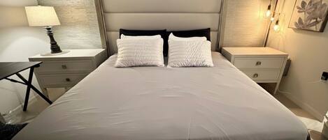Un lit bien fait, avec une tête de lit, deux tables de chevet et une lampe d’un côté.