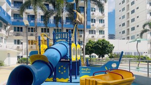 A playground with a slide, climbing structures, and a small yellow vehicle. - Family/Barkada Room 6-10 pax Mall of Asia view Sea Residences  (Pasay)