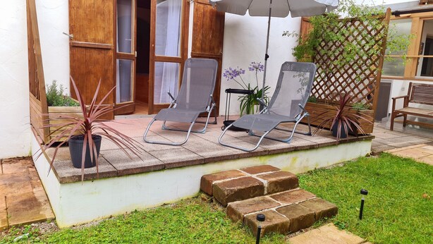 A patio with two lounge chairs, a white umbrella, and a wooden door. - Ruhige Ferienwohnung in Bad Tölz (Bad Tölz)