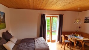 A cozy room with a wooden bed, a dining table with chairs, and a view of greenery outside. - Ruhige Ferienwohnung in Bad Tölz (Bad Tölz)