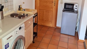 A compact kitchen with a washing machine, a microwave, and wooden cabinets. - Ruhige Ferienwohnung in Bad Tölz (Bad Tölz)
