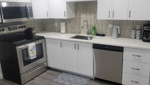 A modern kitchen with stainless steel appliances, white cabinets, a dishwasher, and a coffee maker. - A Cozy home away from home at South East Calgary (Calgary)