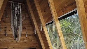 Un dormitori de cabana de fusta amb sostre inclinat, un llit amb almoiners vermells i vista al bosc per una finestra.