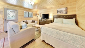 A cozy cabin room with a bed, a sofa, a TV, and a window with blinds. - Fox Creek Cottage located in Panguitch Lake (Panguitch Lake)