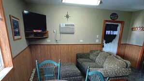 Ein Essbereich mit einem runden Holztisch, blauen Stühlen, einer Couch und einem Fernseher an der Wand.