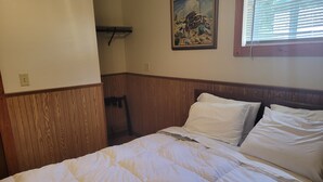 Ein Schlafzimmer mit einem hölzernen Kopfteil, einer weißen Bettdecke und einem Bild an der Wand.
