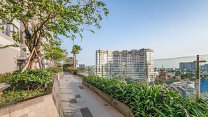 Un chemin bordé de verdure, avec un immeuble de grande hauteur en arrière-plan.