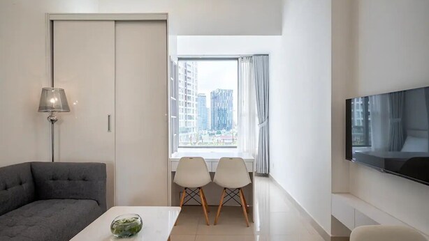 Un salon moderne comprenant un canapé, une table à manger, deux chaises, un téléviseur et une fenêtre donnant sur la ville.