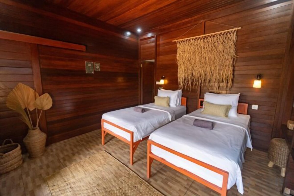 A wooden room with two beds, a woven hanging decoration, and a small basket.