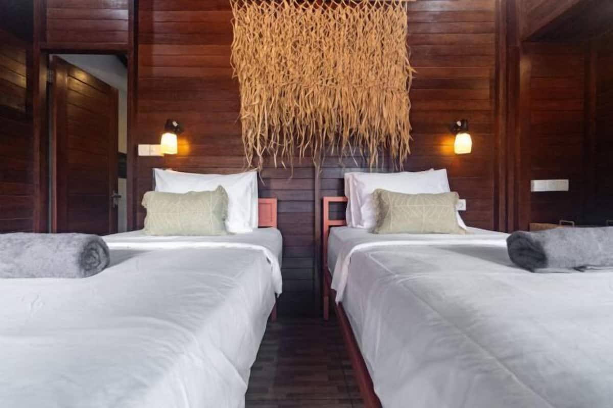 Una habitación con dos camas, paredes de madera y un adorno tejido en el techo.