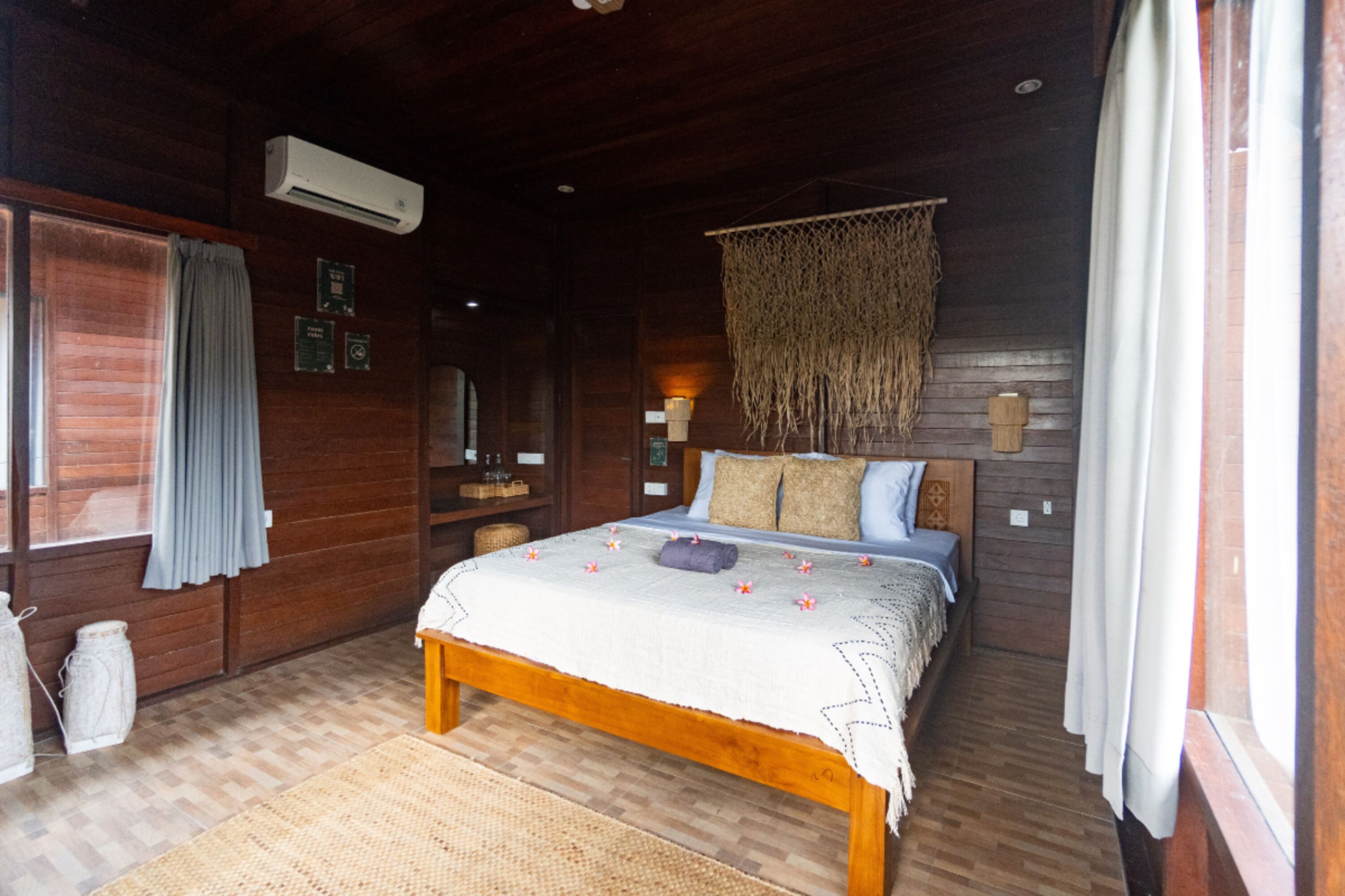 A wooden cabin bedroom with a bed, air conditioning unit, and a hanging macramé decoration.