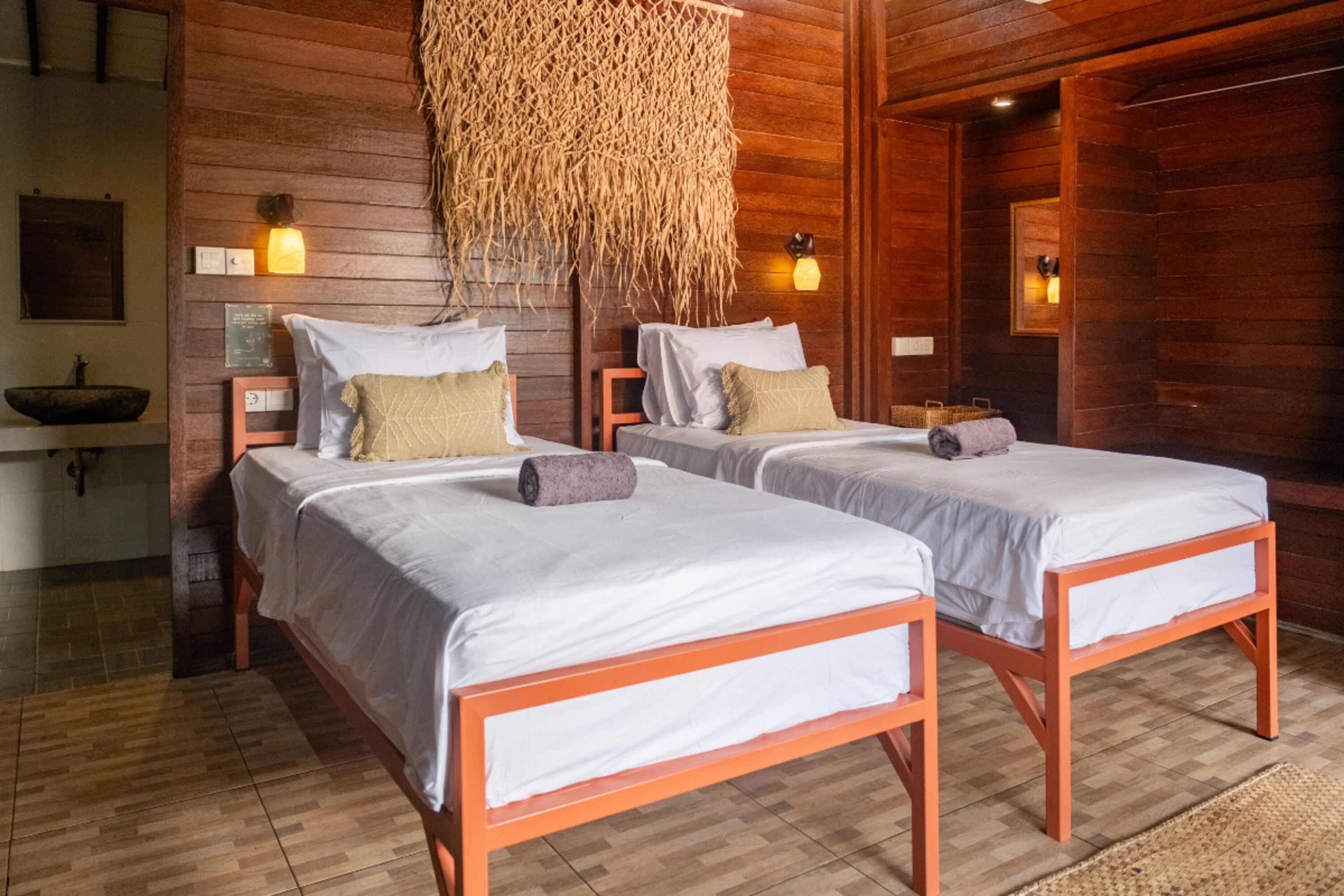 A room with two beds, wooden walls, a woven ceiling, and a small sink.