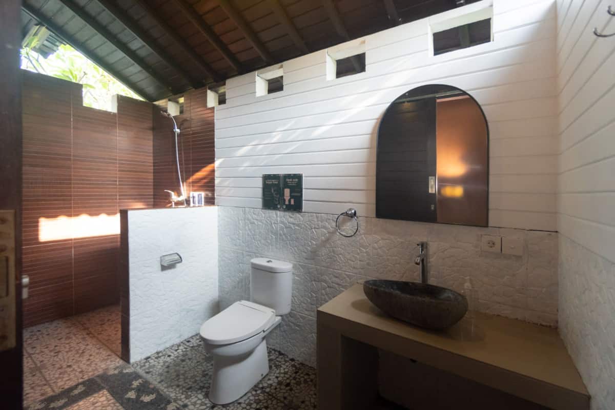 Un baño con inodoro blanco, lavabo de piedra, espejo y ducha.