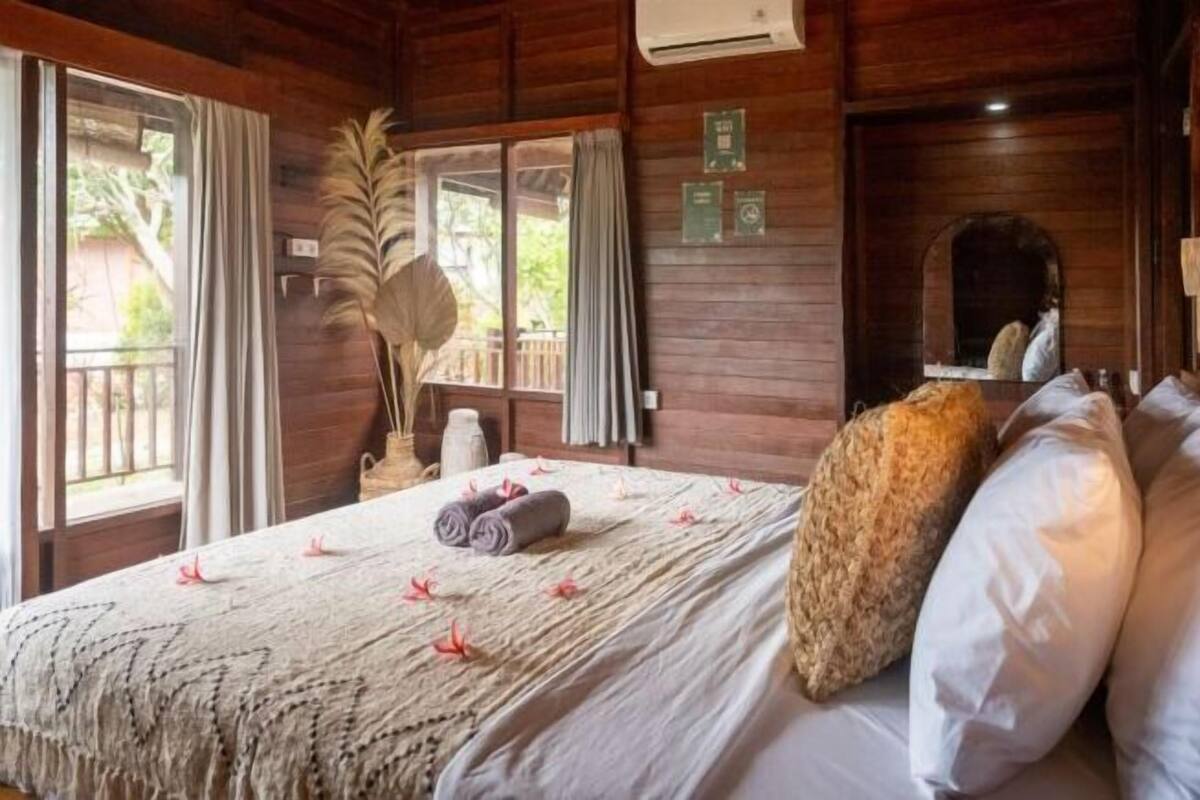 Una habitación de madera con una cama, un espejo y un ventanal con cortinas.