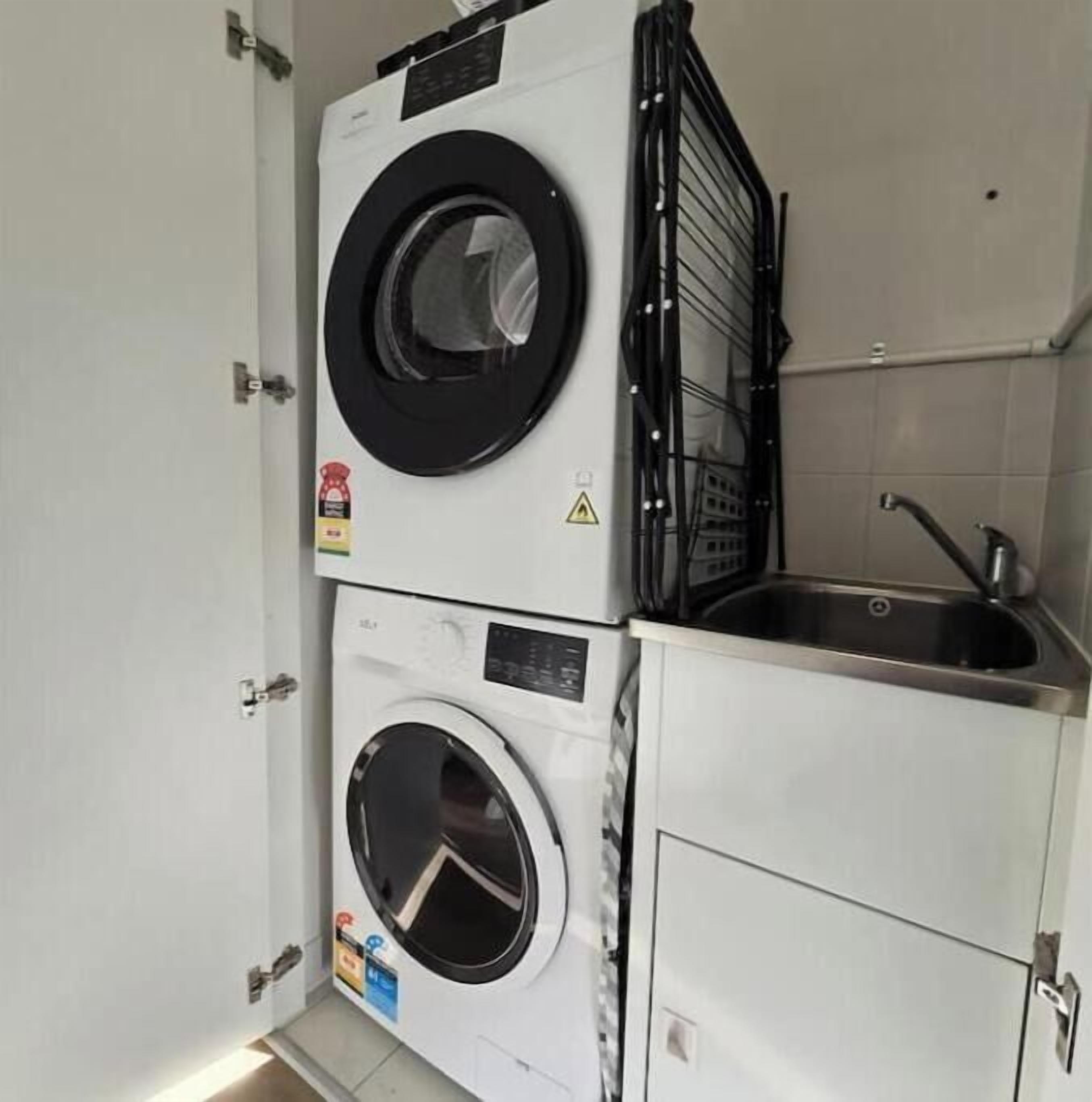 A compact laundry room with a stacked washer and dryer, a metal rack, and a sink.