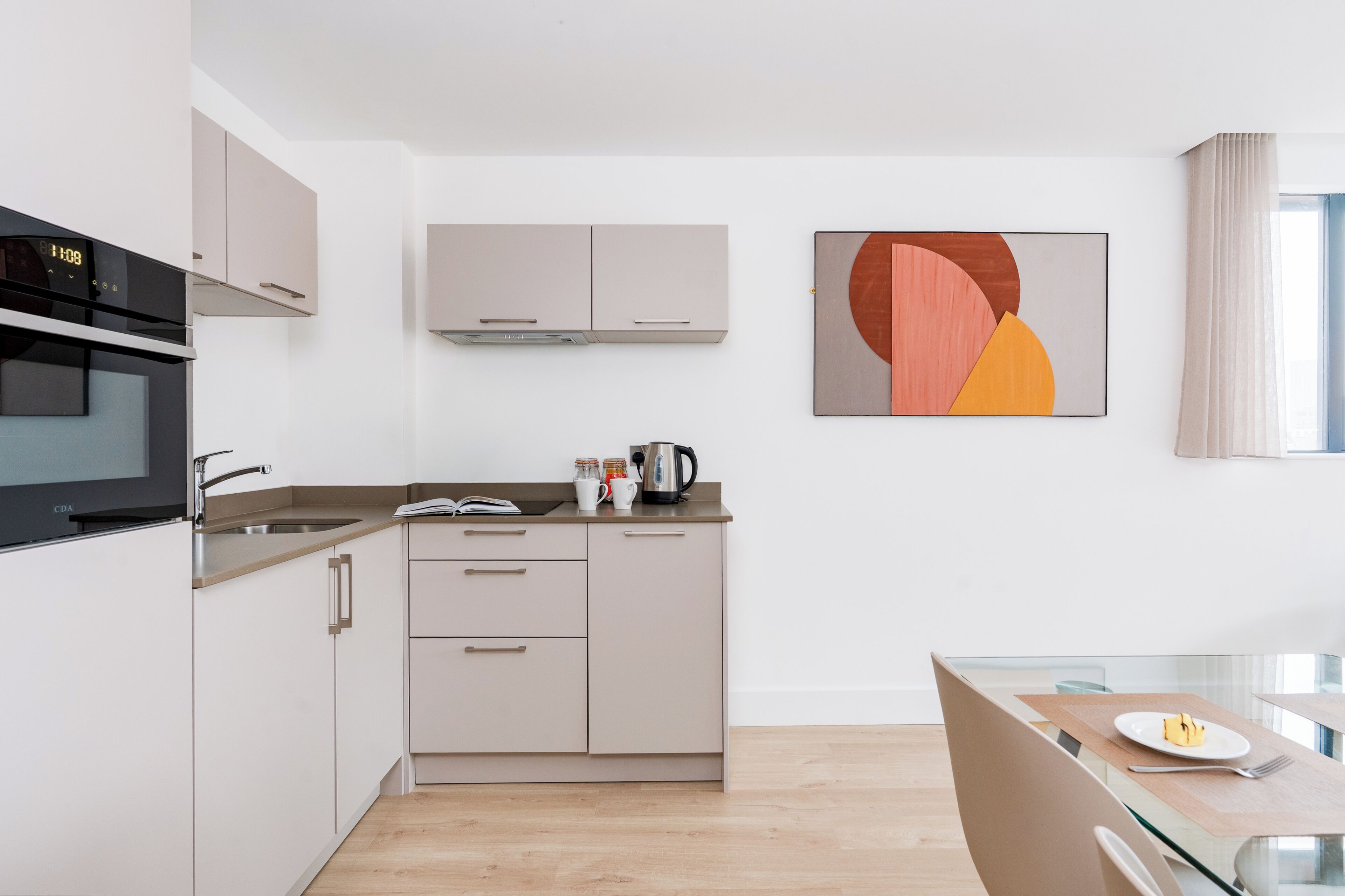Una cocina moderna con horno integrado, cafetera y zona de comedor con mesa y sillas de vidrio.
