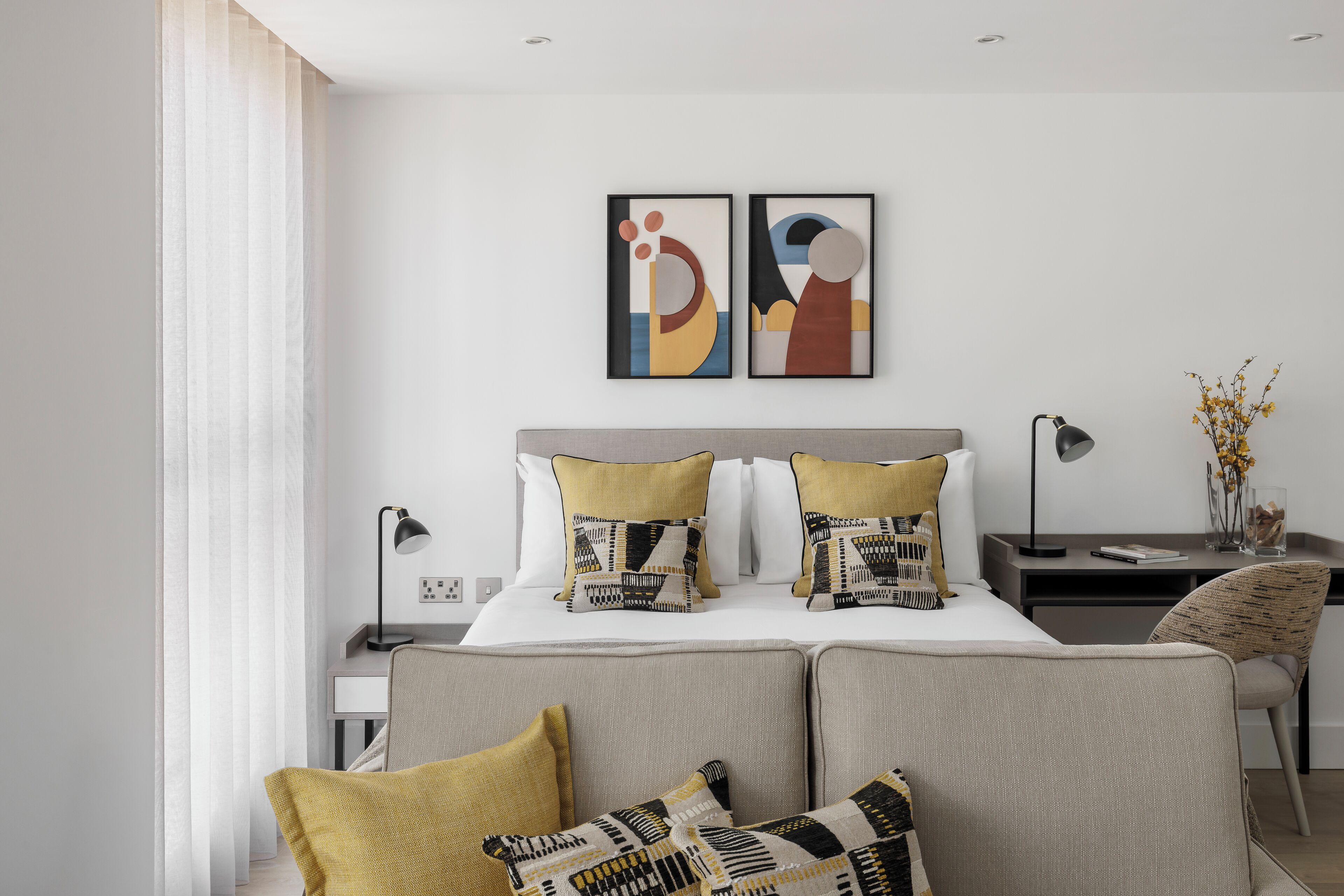 Une chambre à coucher moderne avec un lit, une table de chevet, une lampe et des coussins décoratifs.