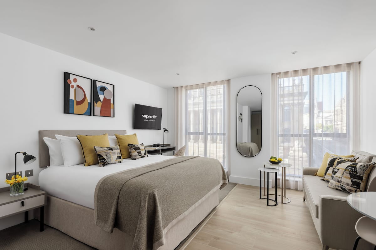 A modern hotel room with a large bed, a sitting area, and a view of the city.