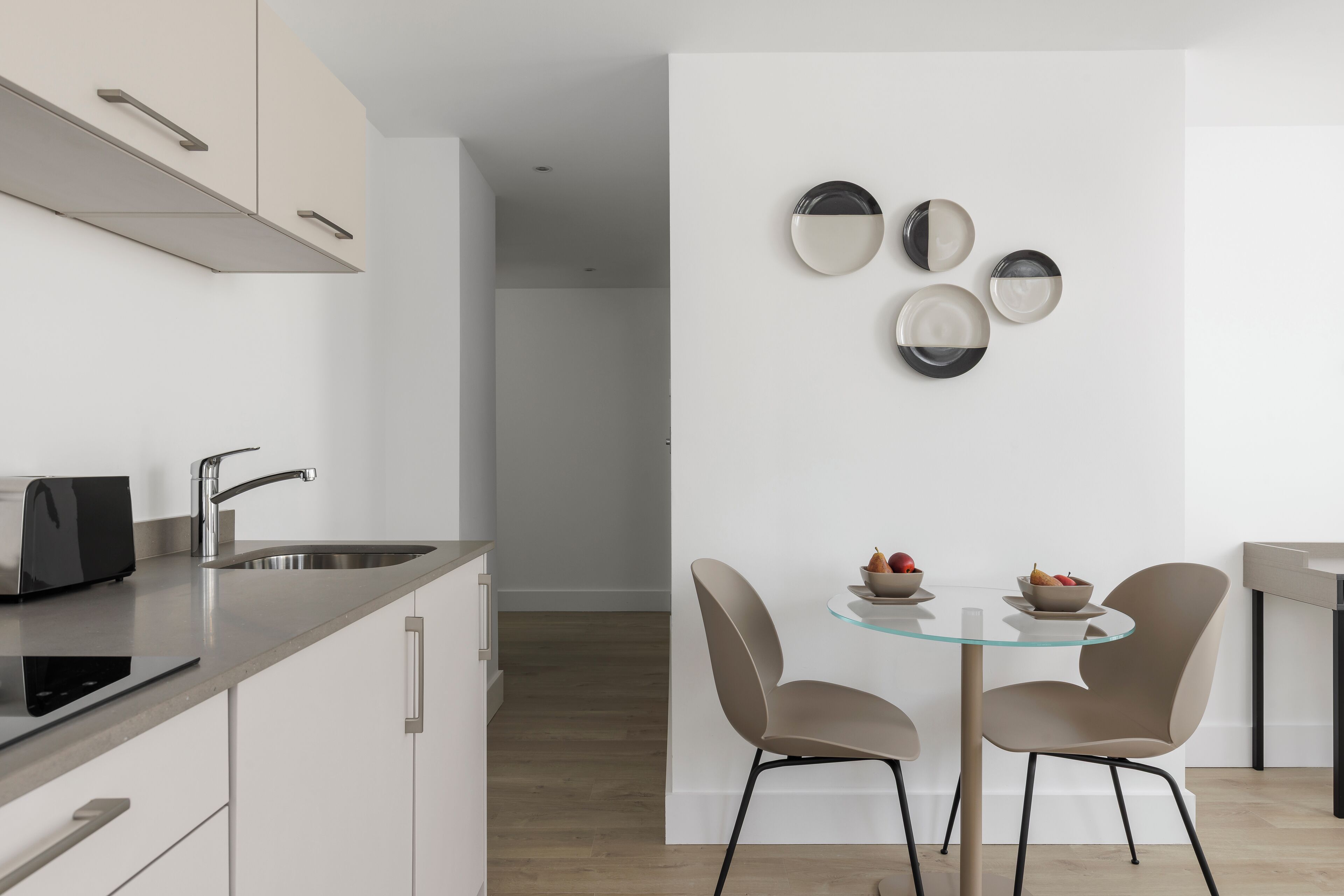 Een moderne keuken met een inbouwtoaster, een roestvrijstalen spoelbak en een eettafel met glazen blad en twee stoelen.
