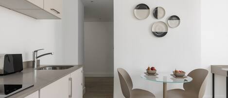 A modern kitchen with a built-in toaster, stainless steel sink, and a glass-top dining table with two chairs.
