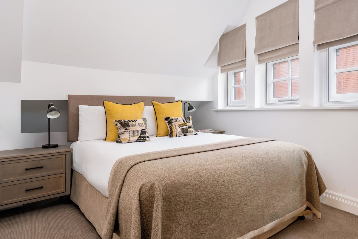 A neatly arranged bedroom with a bed, bedside tables, and a window with curtains.