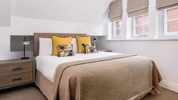Un dormitorio ordenado con cama, mesitas de noche y una ventana con cortinas.