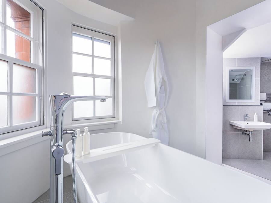 A modern bathroom with a bathtub, a shower, a sink, and a window providing natural light.