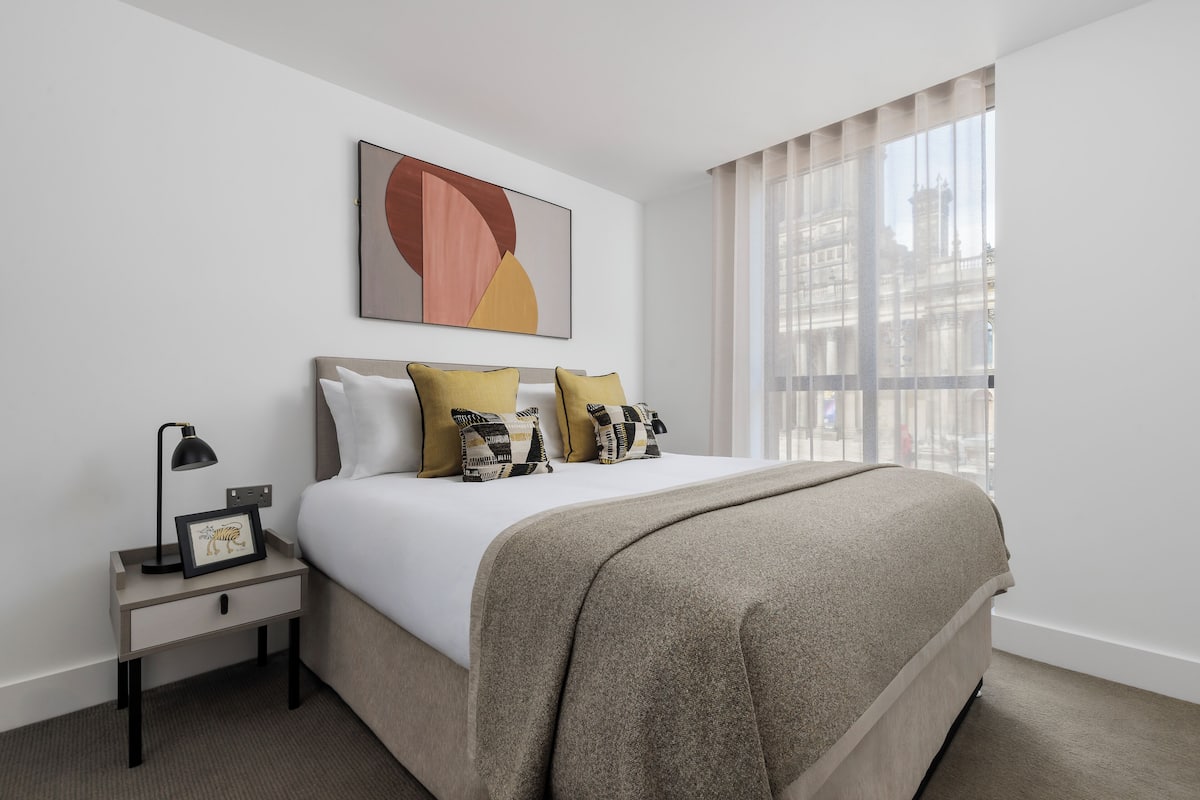 A neatly arranged hotel room with a bed, a nightstand, a framed picture, and a window with curtains.