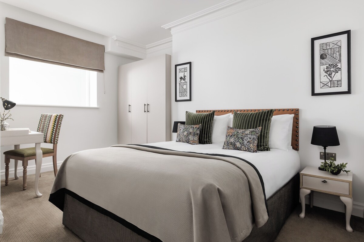 A neatly arranged bedroom with a large bed, bedside tables, a chair, and a desk.