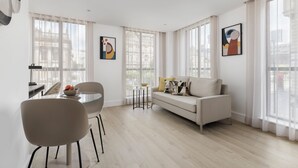 A modern living room with a sofa, a dining table with chairs, and artwork on the walls.