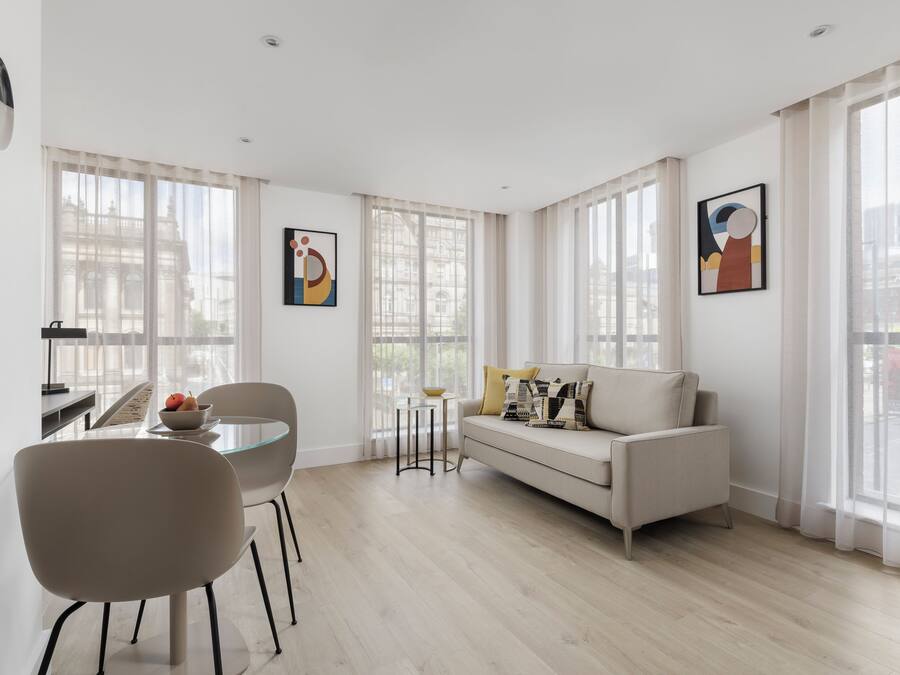 A modern living room with a sofa, a dining table with chairs, and artwork on the walls.