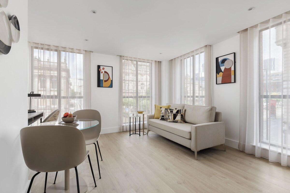 A modern living room with a sofa, a dining table with chairs, and artwork on the walls.
